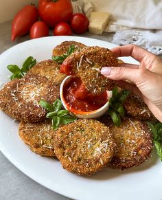 a person dipping sauce on some food on a white plate with tomatoes and spinach