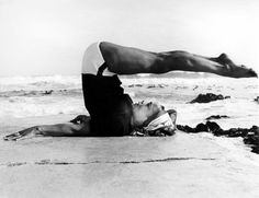 a woman laying on top of a sandy beach next to the ocean with her legs spread out