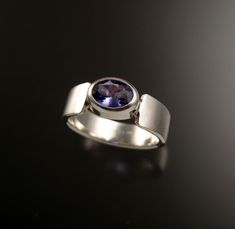 This 5.5 x 7.5 mm Tanzanite oval is bezel-set with tapered cold forged band. The stone is a natural medium dark purple-blue eye clean stone. It weighs about 1ct. Pictured ring is size 7. Specify your ring size in a note to seller at check-out. Modern Oval Tanzanite Sapphire Ring, Modern Oval Amethyst Ring With Polished Finish, Modern Oval Sapphire Ring With Tension Setting, Modern Oval Tanzanite Ring, Gift Sapphire Ring With Oval Tension Setting, Oval Sapphire Ring With Tension Setting As Gift, Oval Ring, Oval Rings, Blue Eye