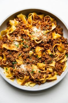 a white bowl filled with pasta covered in meat and sauce on top of a table