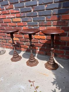 three wooden stools sitting next to a brick wall