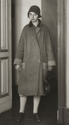 an old black and white photo of a woman in a coat standing at the door