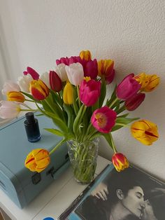 a vase filled with colorful tulips sitting on top of a table next to a book