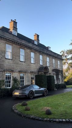 a sports car parked in front of a large house with hedges on both sides and windows