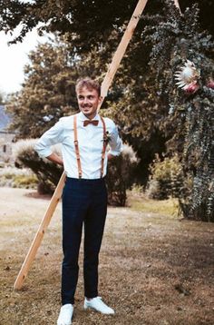 a man in suspenders and bow tie standing next to a pole with birds on it