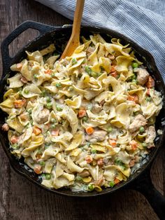 a skillet filled with pasta and vegetables on top of a wooden table next to a blue towel