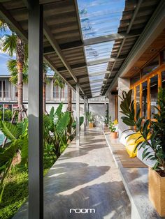 an outdoor covered walkway with plants and potted trees on either side, leading to the pool