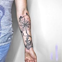 a person with a tattoo on their arm holding a compass and an anchor in the middle