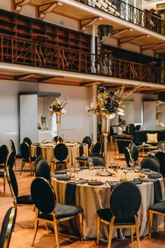 tables with black chairs and gold tablecloths are set up in the middle of a large room