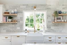 a kitchen with white cabinets and marble backsplash, open shelving above the sink