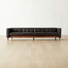 a black leather couch sitting on top of a hard wood floor next to a white wall