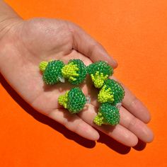 a person's hand holding four tiny broccoli pieces on an orange background