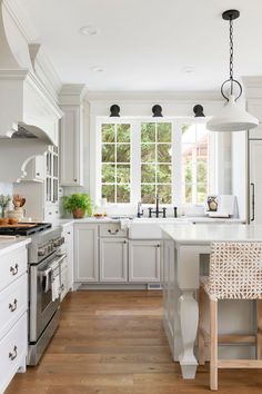 a kitchen with white cabinets and wood flooring next to a stove top oven in front of a window