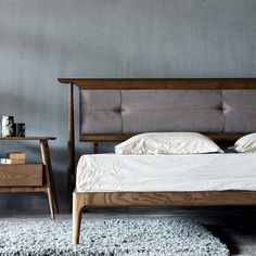 a bed sitting on top of a white rug next to a night stand and table