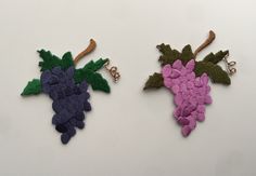 two pieces of crocheted fabric with leaves and grapes attached to them on a white surface