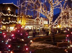 christmas lights on trees and buildings in the background at night with people walking around them