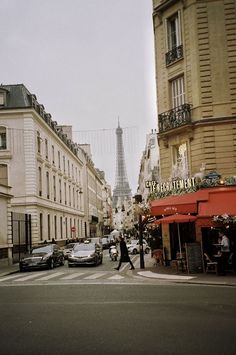 the eiffel tower is seen in the distance from this street corner with parked cars