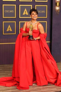 a woman in a red gown holding an award and posing for the camera with her hands on her hips