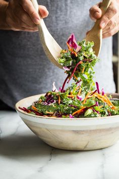 a person holding a wooden spoon over a salad