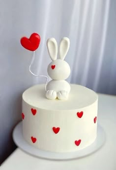 a white cake decorated with red hearts and a bunny holding a heart balloon on top