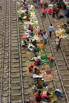 many people are standing on train tracks with food and vegetables laid out in the middle