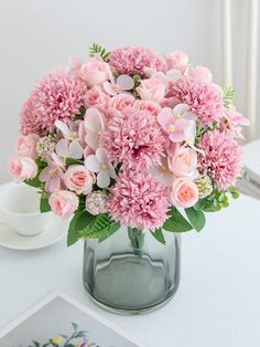 a vase filled with pink flowers sitting on top of a table next to a cup and saucer