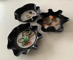 three black bowls filled with coins and scissors on top of a white table next to each other