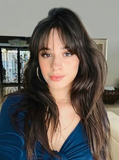 a woman with long brown hair and blue shirt in a living room looking at the camera