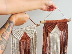 two handmade macrame hangings with tassels and wood sticks, one being held by a woman's arm