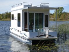 a houseboat floating on top of a lake next to tall grass and trees in the background