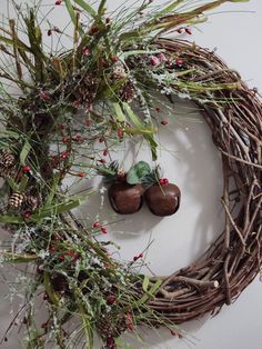 a wreath with two shoes hanging from it and pine cones on the front, surrounded by greenery