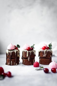 three small cakes with chocolate frosting and cherries on top, surrounded by cranberries