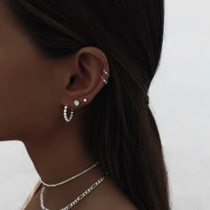 a close up of a woman wearing two necklaces and one earring with pearls