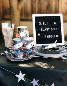 a table topped with plates and cups filled with cake next to a sign that says blast off