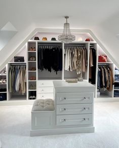 a white closet with drawers and clothes hanging on the walls, under a slanted ceiling