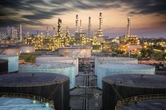 an oil refinery at night with lots of tanks in the foreground and city lights in the background