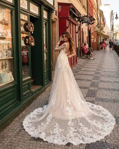 a woman standing in front of a store wearing a wedding dress with long sleeves and an open back