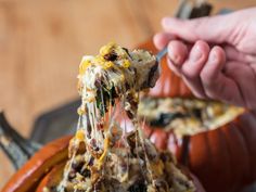 a person holding a spoon full of food in their hand and eating it out of a pumpkin