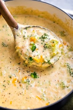 a ladle full of broccoli cheese soup being stirred with a wooden spoon