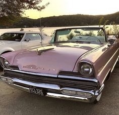 two old cars parked next to each other in a parking lot near the water at sunset