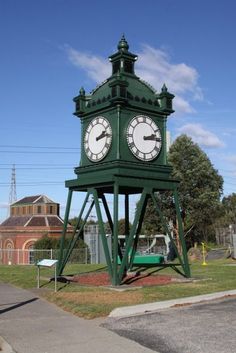 a large green clock tower sitting on the side of a road next to a park