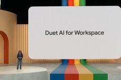 a man standing on top of a stage next to a giant sign that says duet al for workspace