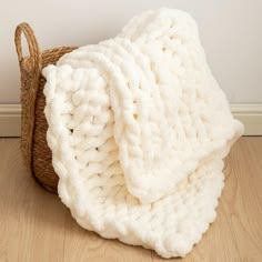 a white knitted blanket sitting on top of a wooden floor next to a basket