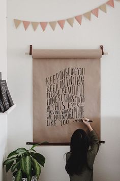 a woman writing on a wall with a quote above her head and some books in the background