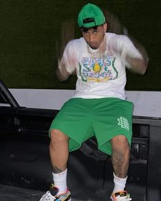 a man sitting on the back of a truck wearing green shorts and a white t - shirt