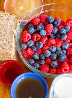 a bowl filled with raspberries and blueberries next to bread