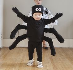 a young boy is standing in front of a giant spider costume with two smaller boys behind him