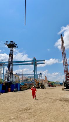 a little boy standing in the middle of a dirt field next to construction equipment and cranes