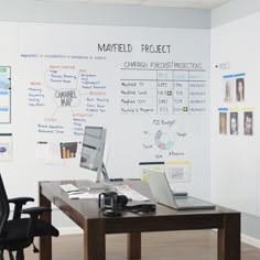 a desk with a laptop computer on top of it next to a whiteboard covered wall