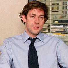 a man wearing a blue shirt and black tie sitting in front of a computer monitor